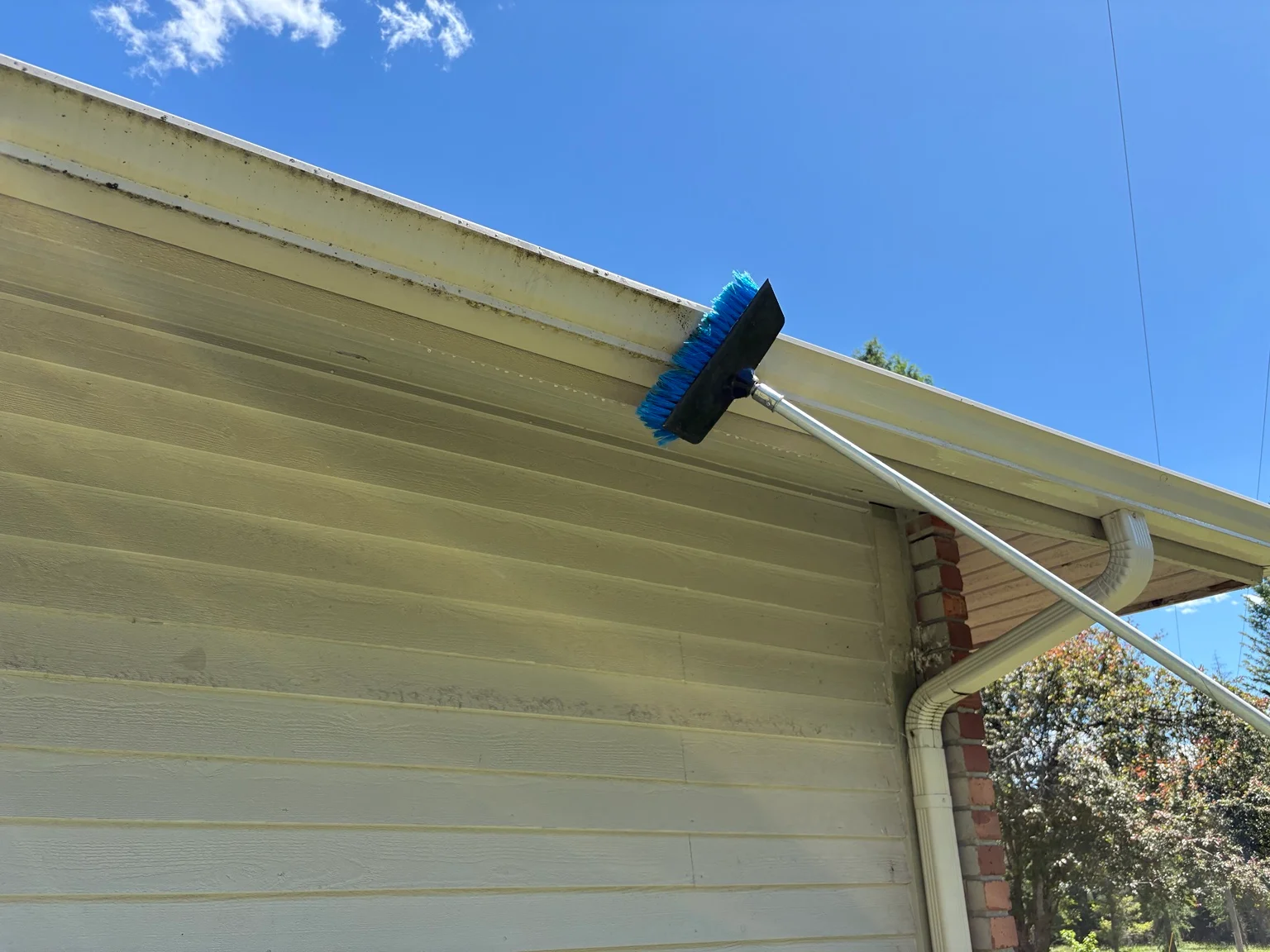 Pressure washing brush cleaning cream-colored soffit and fascia on residential home