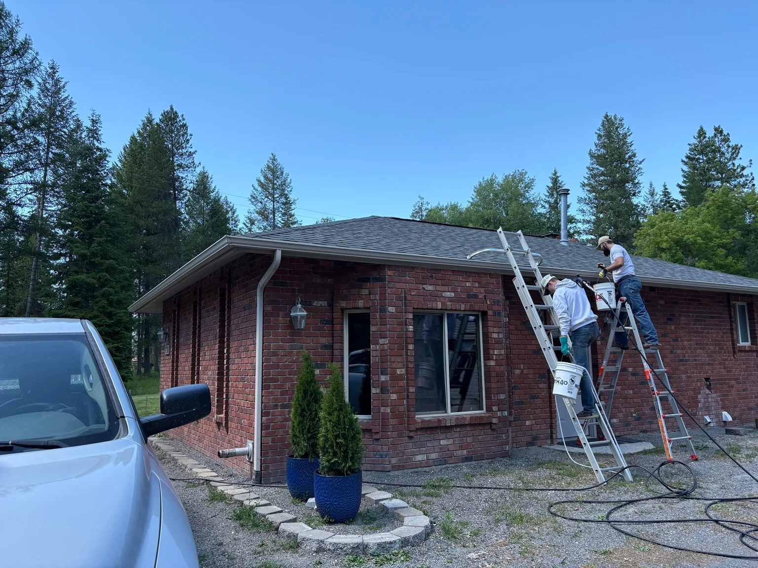 Technicians pressure washing and cleaning gutters on red brick home with extension ladders
