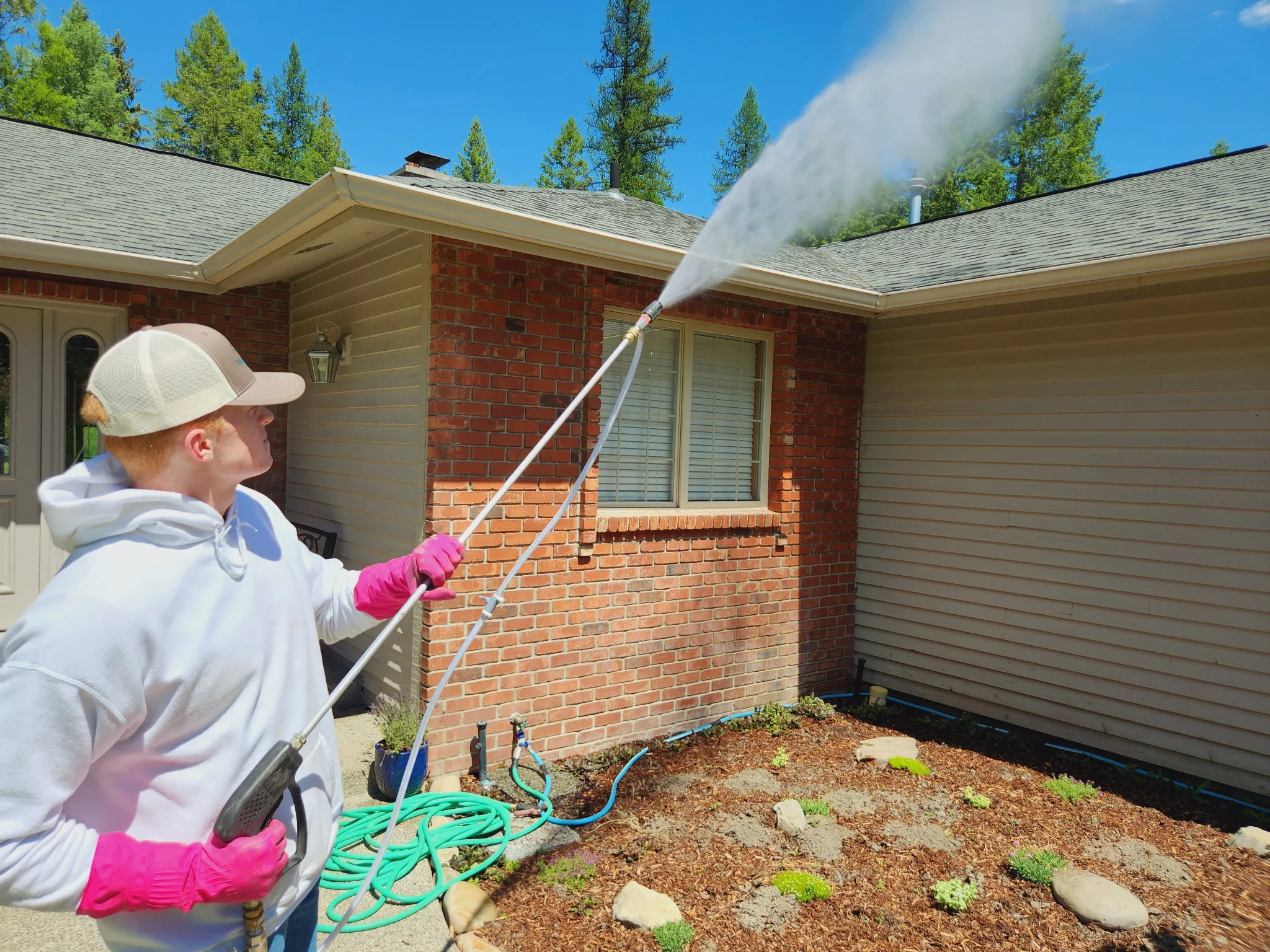 Technician pressure washing red brick and tan siding on residential home exterior