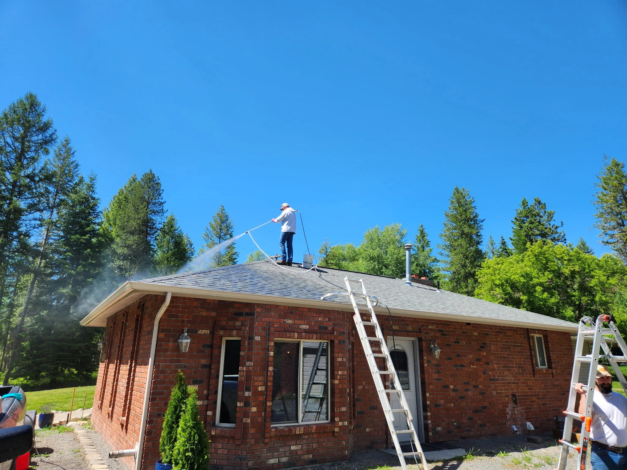 Technician pressure washing brick home roof with extension ladder and spray equipment