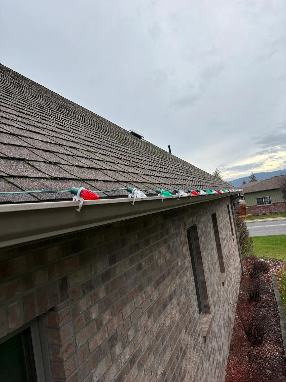 Installed gutters with colorful downspout extensions on residential brick home roofline