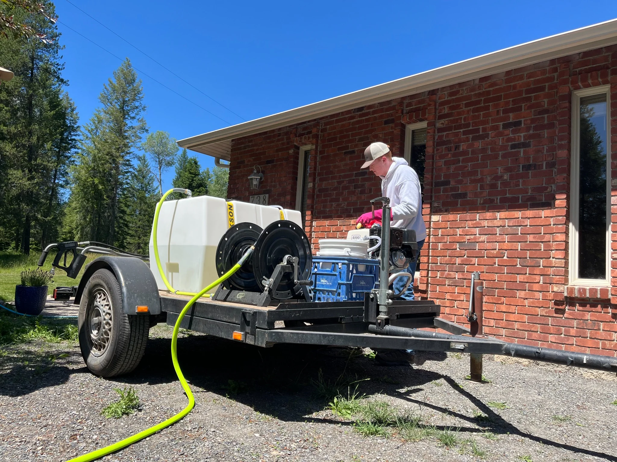 Technician operating pressure washing equipment on red brick home exterior in Colville