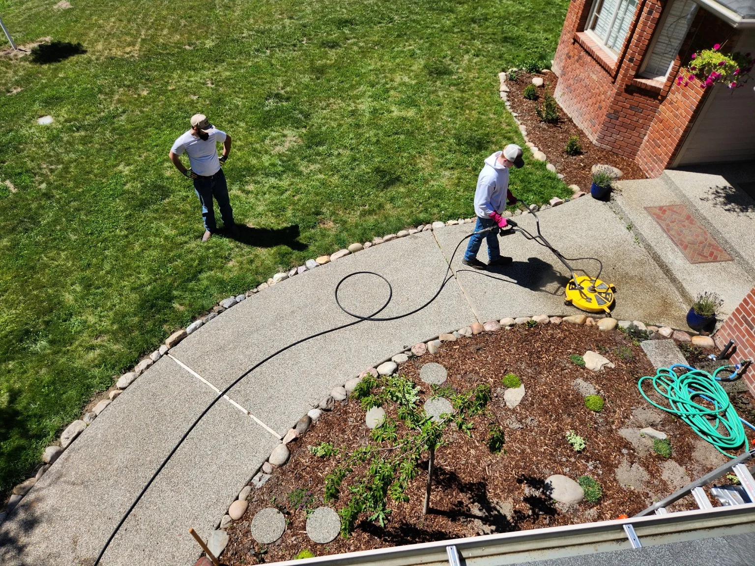 Technician pressure washing residential driveway with yellow equipment and hose