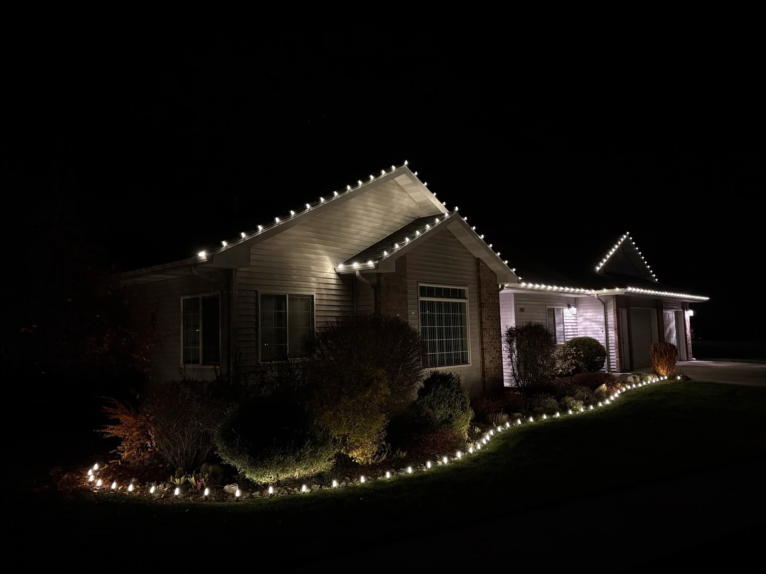 Home exterior at night with white LED lights outlining roofline and landscaping