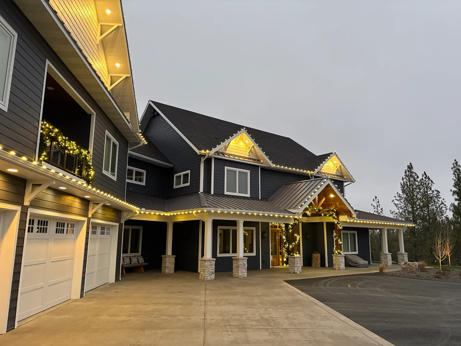 Modern farmhouse with warm-white holiday lights on roofline, gables, and porch at dusk