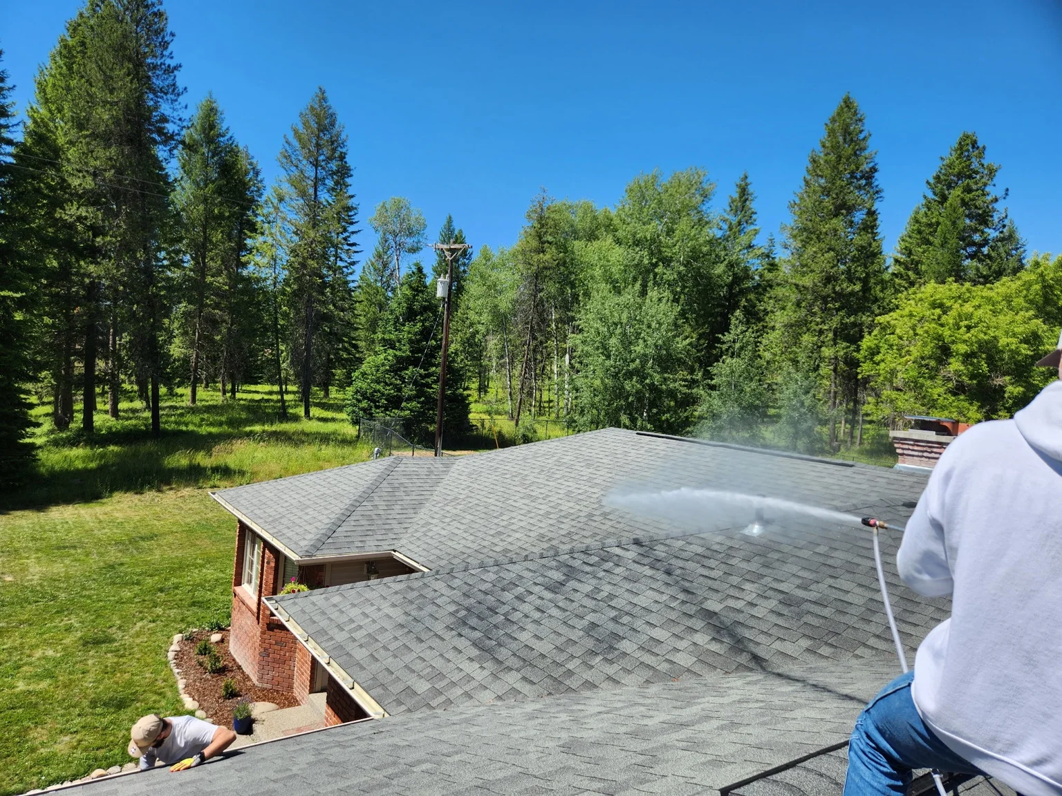 Technician pressure washing residential roof with forest backdrop in Colville, WA