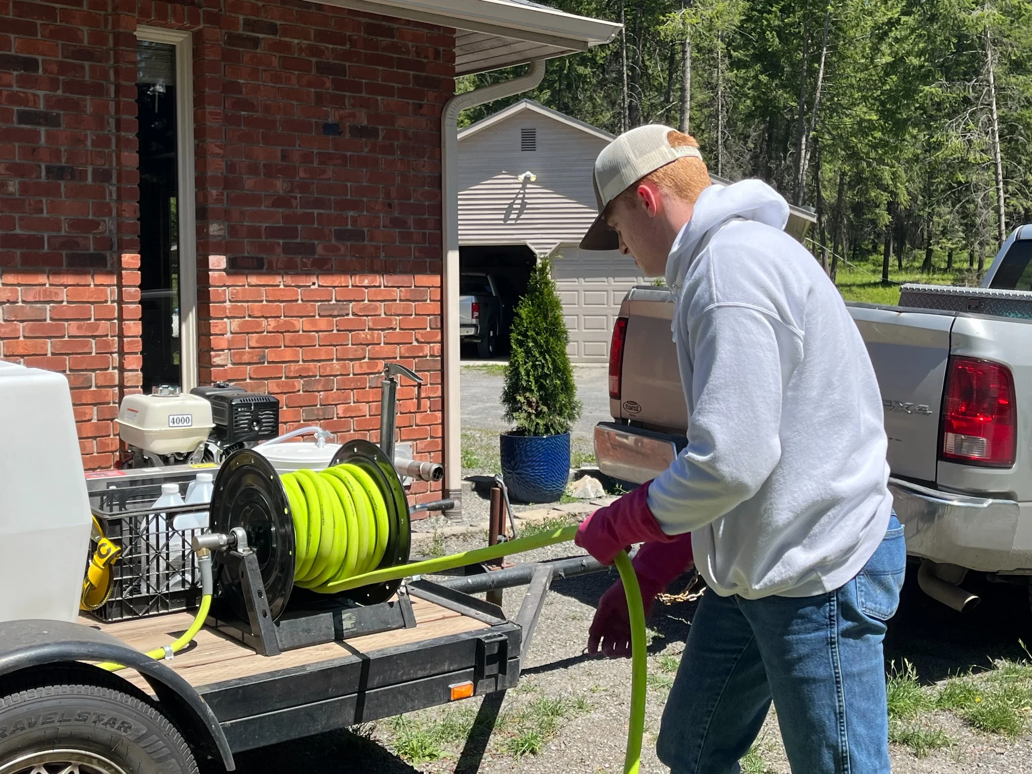 Technician with pressure washing equipment and yellow hose reel at residential brick home