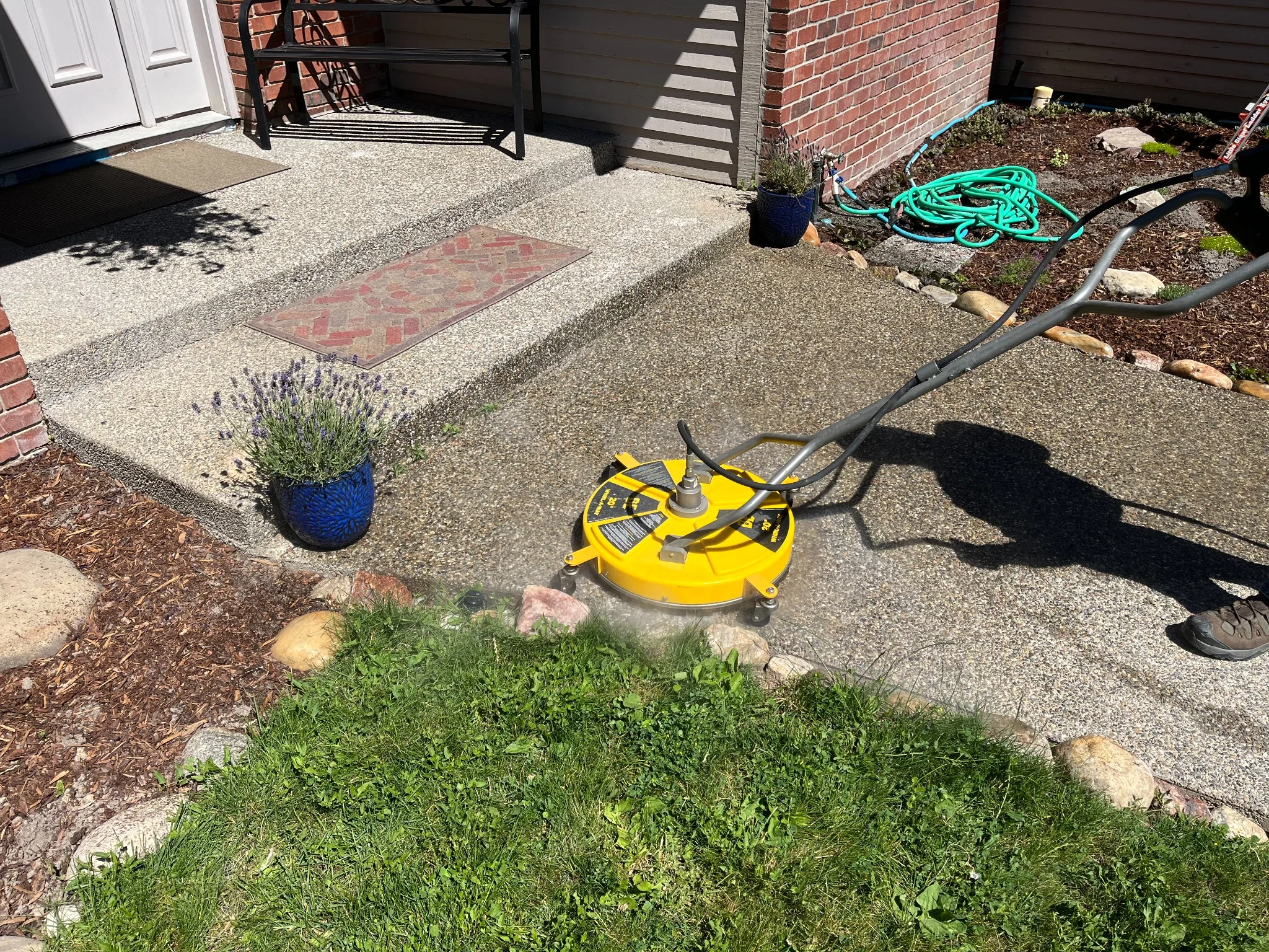 Yellow pressure washer cleaning concrete driveway in front of brick home