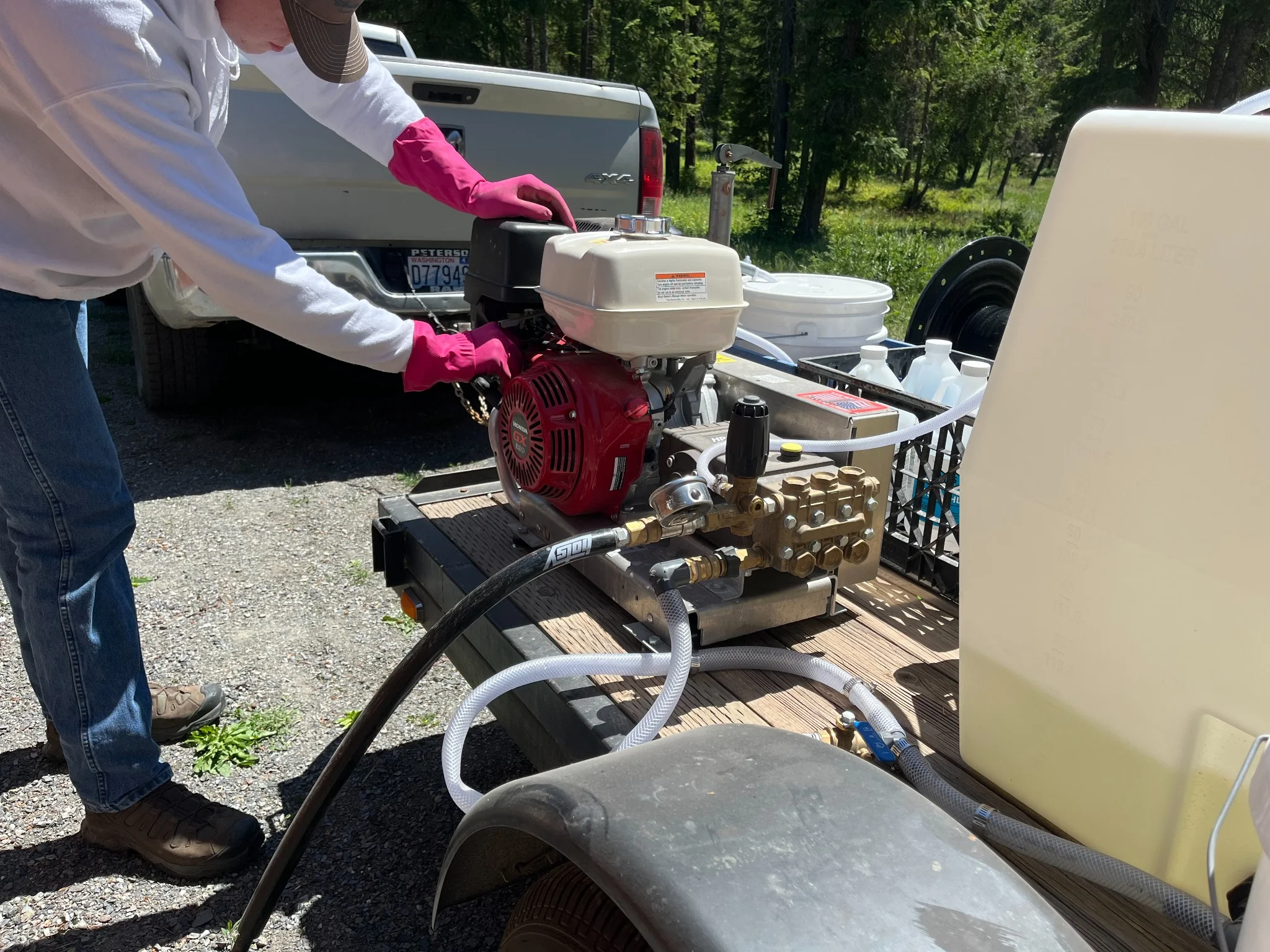 Technician operating professional pressure washing equipment with gas engine and water tanks on trailer