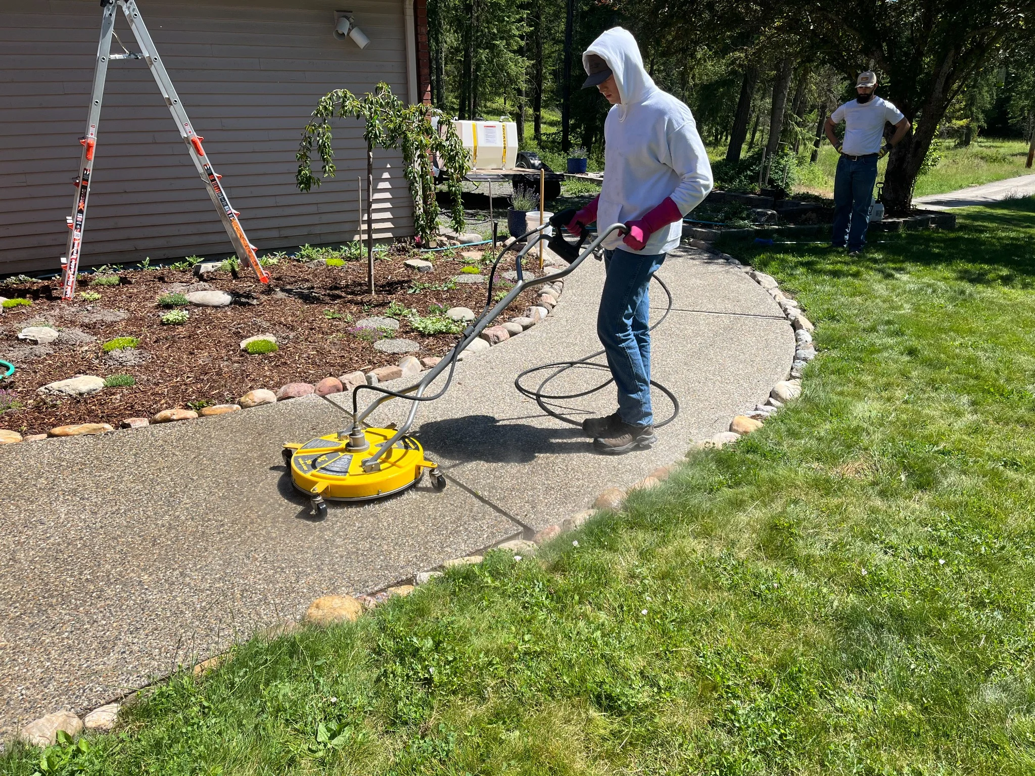 Technician pressure washing concrete pathway with yellow surface cleaner equipment