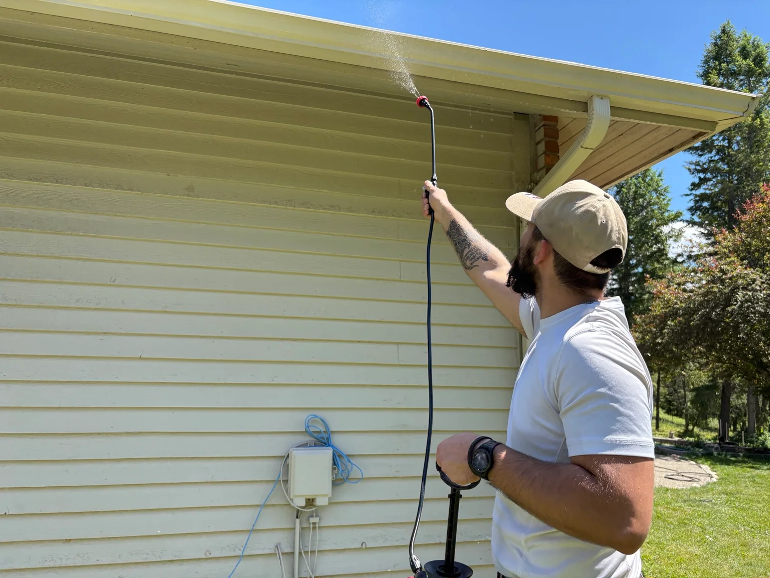 Technician pressure washing cream-colored vinyl siding on residential home exterior