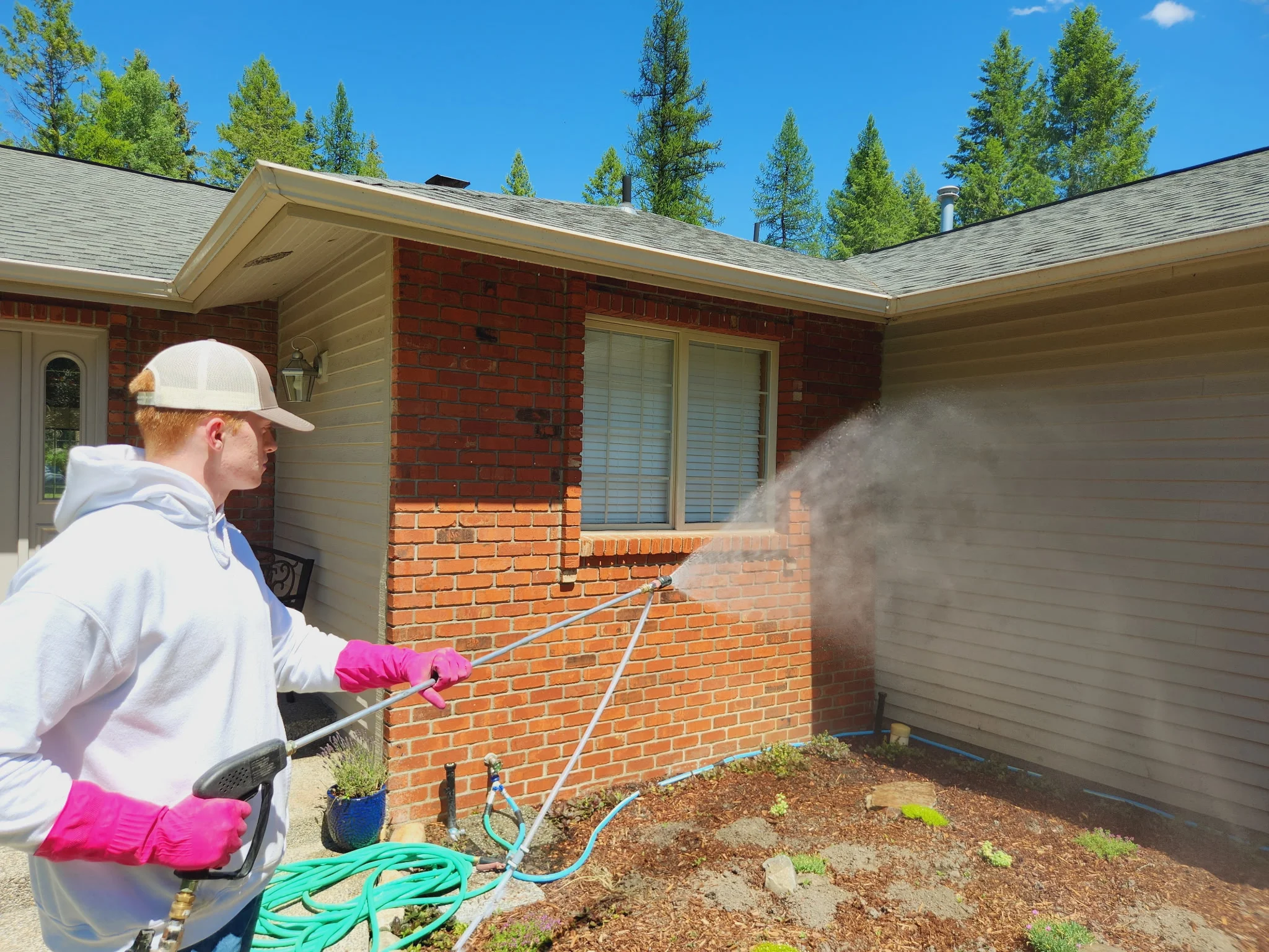 Technician pressure washing red brick home exterior with high-pressure equipment