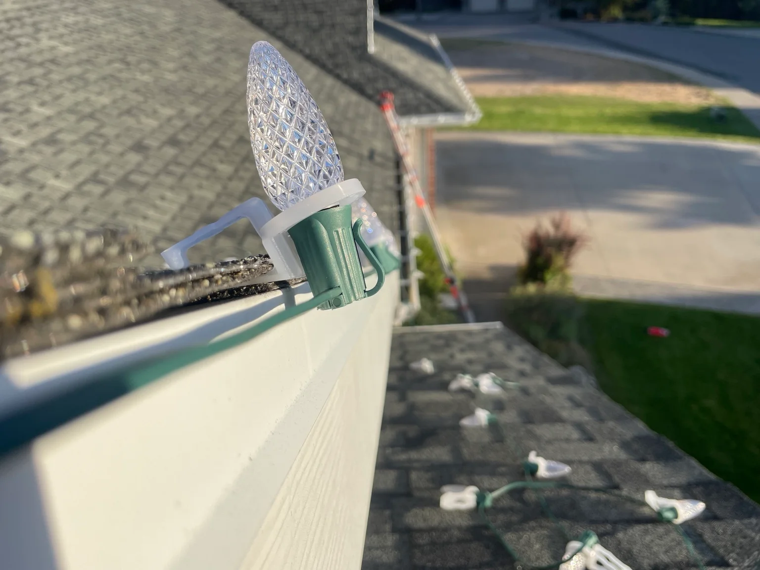 LED Christmas lights installed along white gutter with green wire clips
